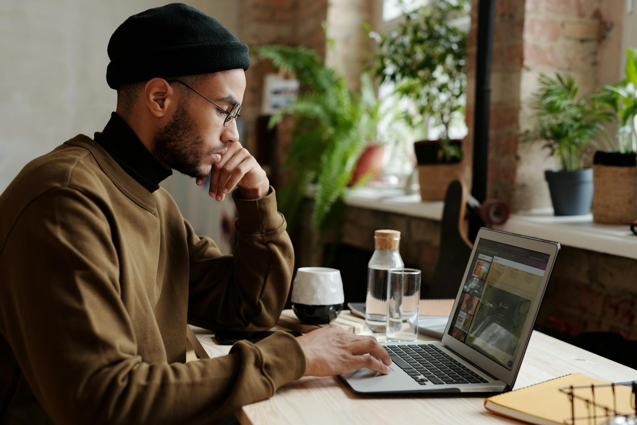 A stylish young man works remotely on his laptop in a cozy indoor workspace.